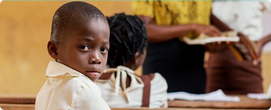 A young boy sitting in a rural classroom looking back with a longing expression, representing the education crisis and the UNESCO 2026 Education Monitoring Report findings.
