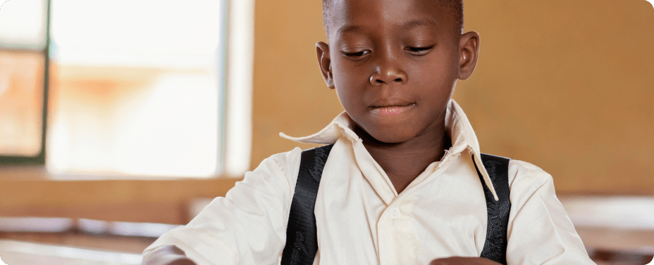 A young African boy sitting at his desk in a classroom, showing how education creates a future beyond the streets and fosters academic focus.