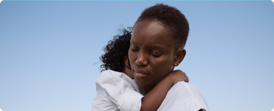Close-up portrait of an African mother’s face while holding her baby, representing the shield of safety and maternal love in rural communities.