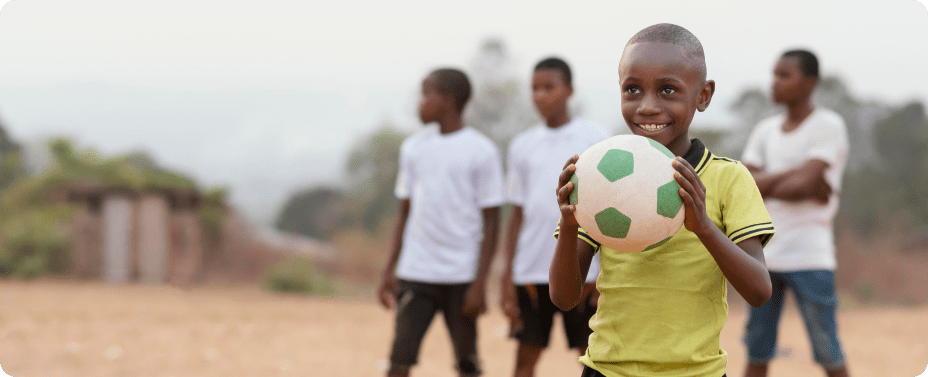 A smiling young African boy holding a football, representing successful youth development through sports in Africa and emotional healing.