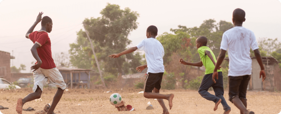 A group of young African boys playing football together on a local field, showcasing the impact of youth development through sports in Africa.