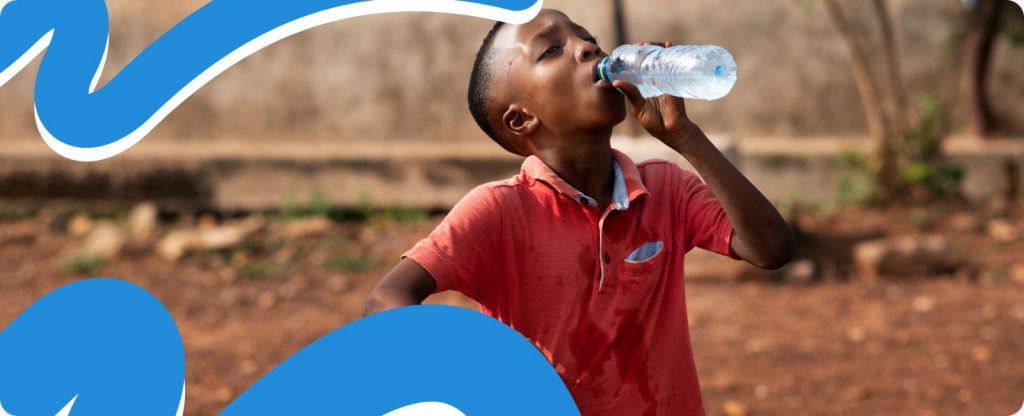 A young boy happily drinking from a bottle of safe water, illustrating the life-saving results of clean water and sanitation in Africa.