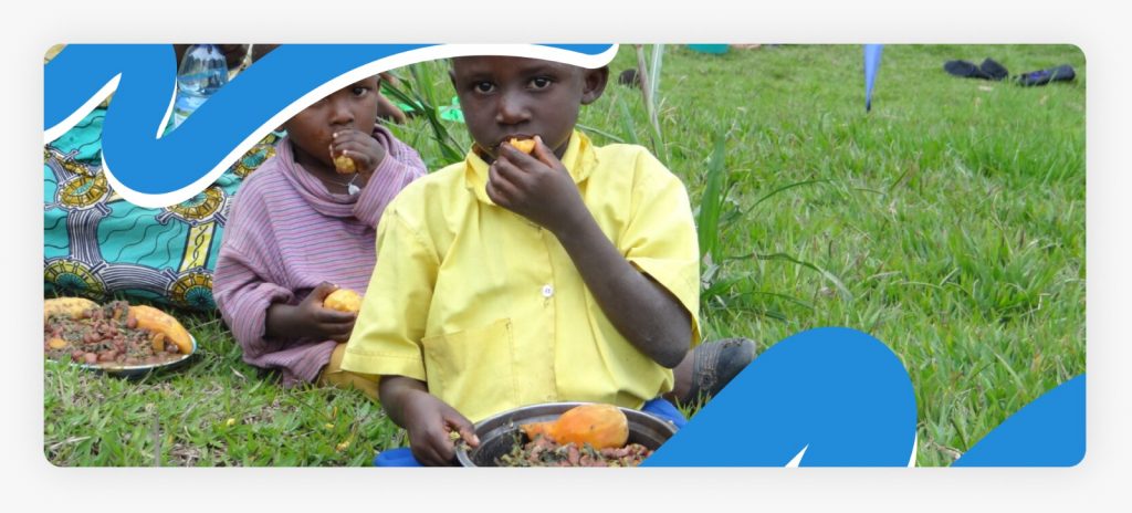 A group of children sitting together in a field and eating nutritious meals, showing the successful recovery of malnourished children in Africa through donor-funded feeding programs in 2026.