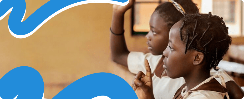 Two students eagerly raising their hands to answer a question in a classroom, representing the growth of economic literacy and ending poverty in rural Africa 2026.