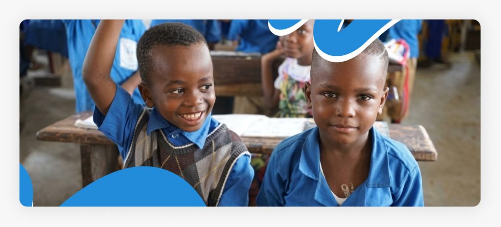 Two happy children smiling together inside a safe classroom, demonstrating the joy found through education for children in conflict zones in Africa.