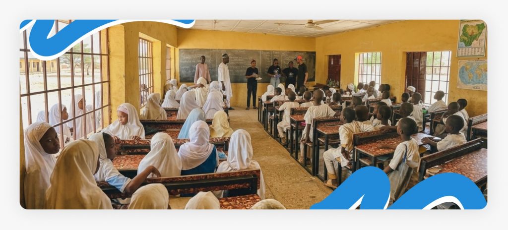 Happy primary school kids sitting and standing as they collect new books from Better Life NGO outreach staff, celebrating how impactful education can be in Africa.