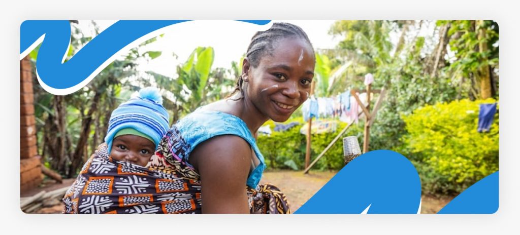 A smiling mother carrying her baby on her back in a traditional wrap, symbolizing the restoration of hope and dignity for families in rural Africa in 2026.