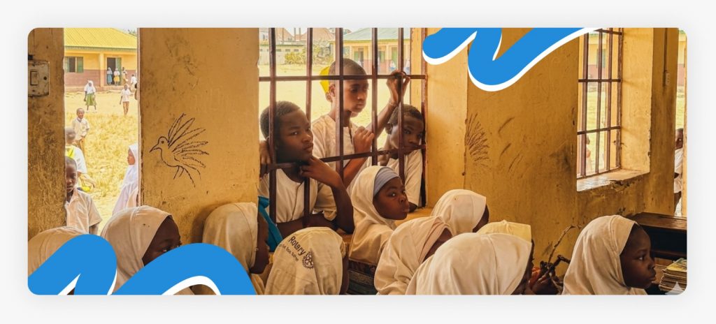 Primary school children standing outside and looking through a classroom window due to a lack of benches and primary school support in Africa.