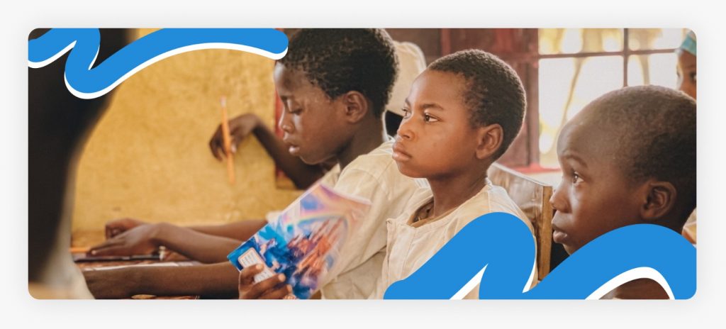 Three primary school students sitting attentively at their desk in class, enduring a system with a lack of enough teachers because there is no enough funds to pay the teachers.