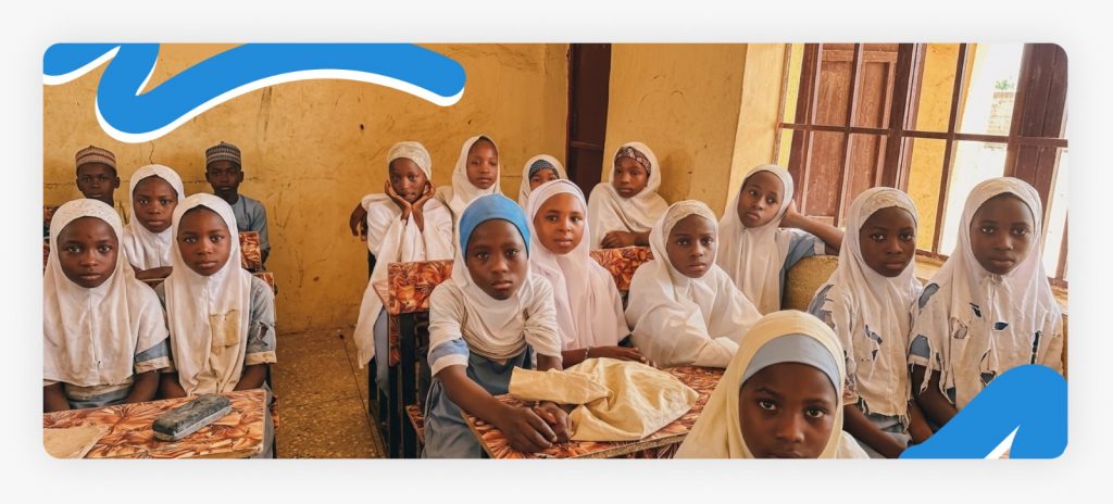 Two primary school students sitting down at their desk in the classroom with torn uniforms, highlighting the fact that most children had worn thorn uniforms due to extreme poverty.
