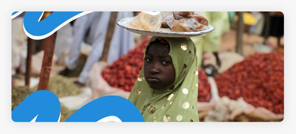 A young African girl standing on the street while balancing a vending tray on her head to sell goods, highlighting the cycle of poverty that requires support for out of school children in Africa.